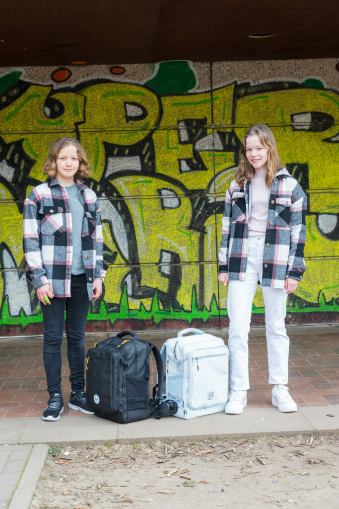 Die Zwillinge Lisa und Nele stehen mit ihrem Schulrucksack von Kattbjoern vor einer gelben Graffitiwand